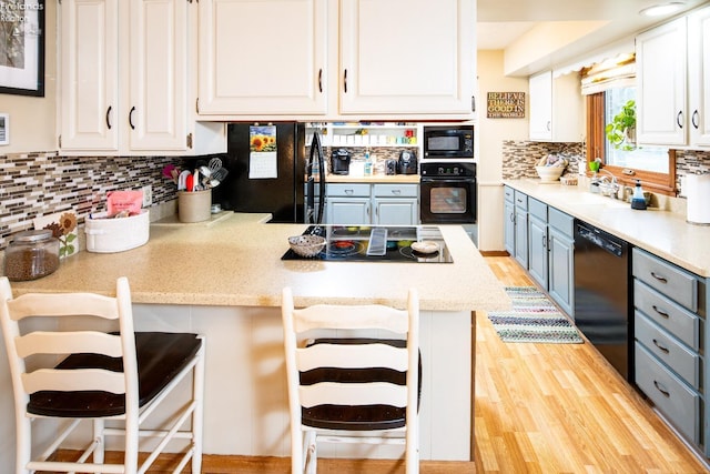 kitchen with white cabinetry, a sink, light wood-type flooring, a peninsula, and black appliances