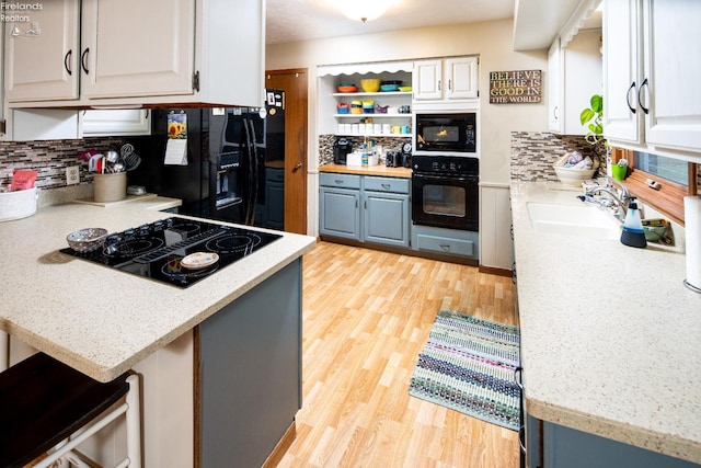 kitchen featuring black appliances, light wood-style flooring, backsplash, and a sink