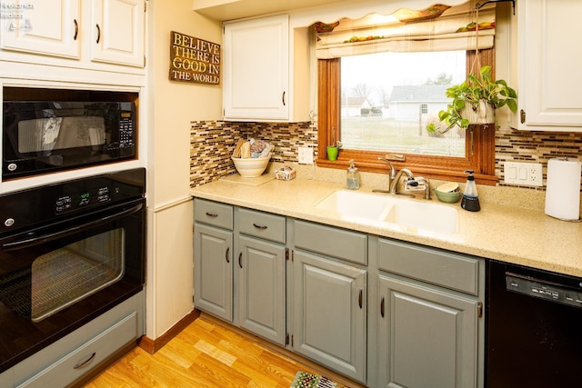 kitchen with white cabinets, light wood-style floors, gray cabinetry, black appliances, and a sink