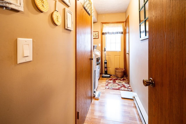 corridor with a baseboard heating unit, light wood-style flooring, and baseboards