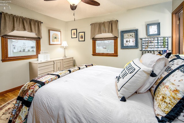 bedroom with a textured ceiling, wood finished floors, a ceiling fan, and baseboards