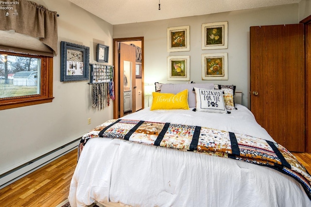 bedroom with ensuite bath, baseboard heating, and wood finished floors