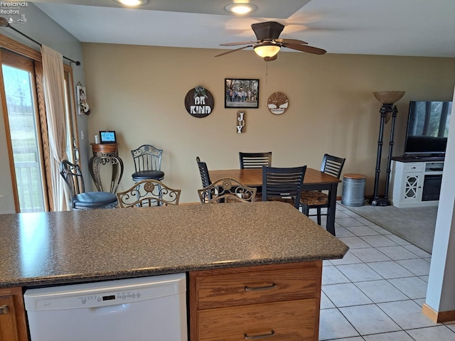 kitchen with brown cabinets, dark countertops, light tile patterned flooring, ceiling fan, and dishwasher