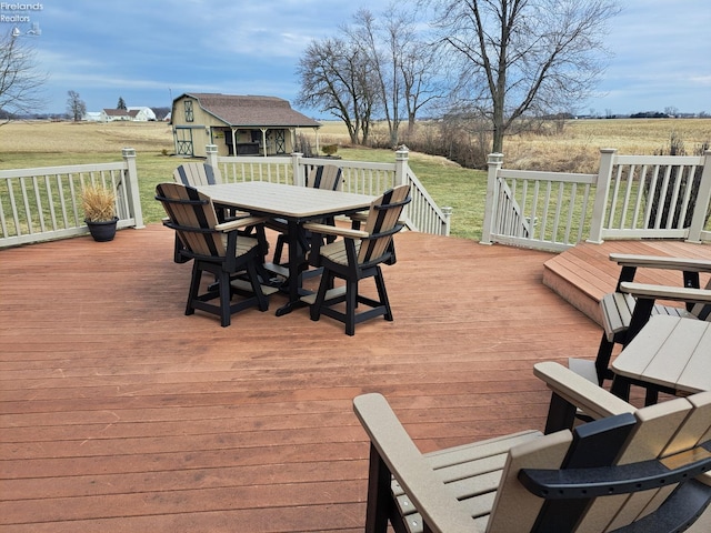 deck featuring a rural view, outdoor dining area, a lawn, and an outbuilding