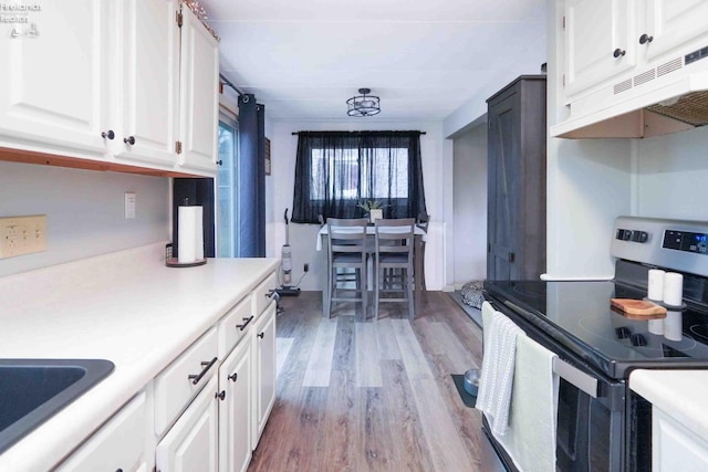 kitchen with under cabinet range hood, light wood-style flooring, light countertops, and electric stove