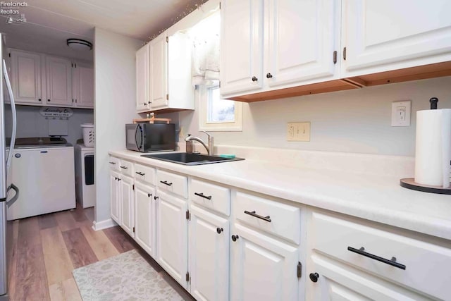 kitchen with a sink, separate washer and dryer, white cabinets, black microwave, and light countertops