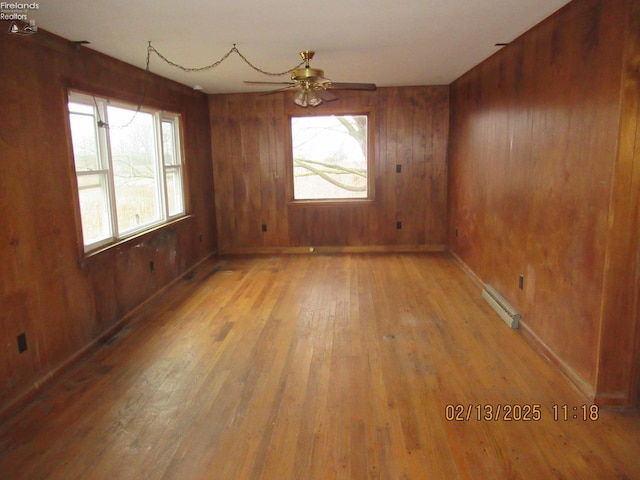 empty room featuring light wood finished floors, a baseboard radiator, a ceiling fan, and a wealth of natural light