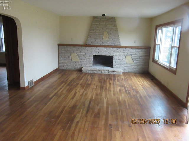 unfurnished living room with arched walkways, a fireplace, visible vents, wood finished floors, and baseboards