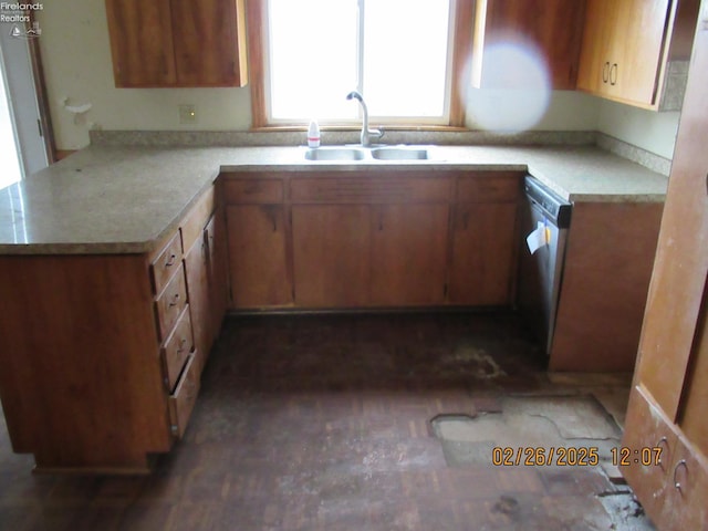 kitchen with brown cabinets, light countertops, stainless steel dishwasher, a sink, and a peninsula