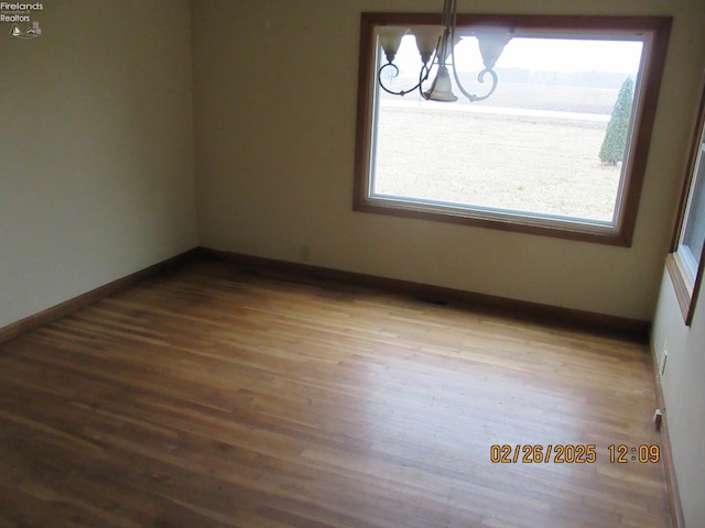 unfurnished room featuring a chandelier, plenty of natural light, wood finished floors, and baseboards