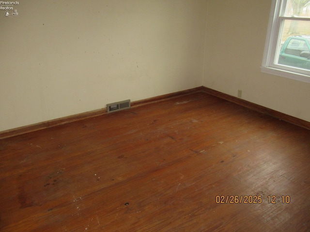 unfurnished room with hardwood / wood-style floors, visible vents, and baseboards