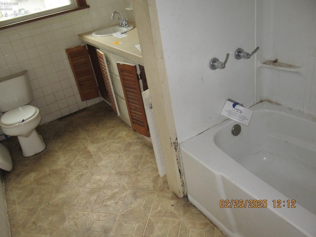 bathroom featuring toilet, tile patterned floors, a bathtub, vanity, and tile walls