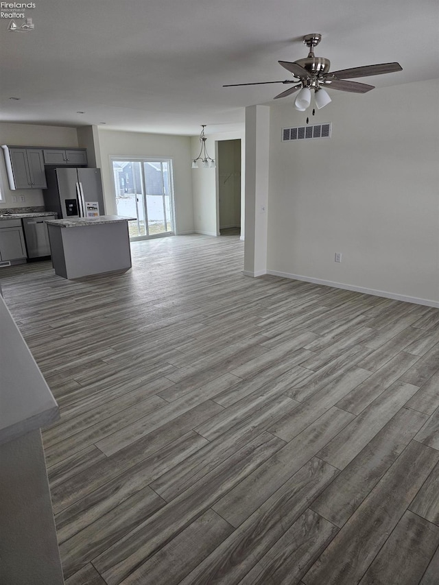 unfurnished living room with a ceiling fan, dark wood-style flooring, visible vents, and baseboards