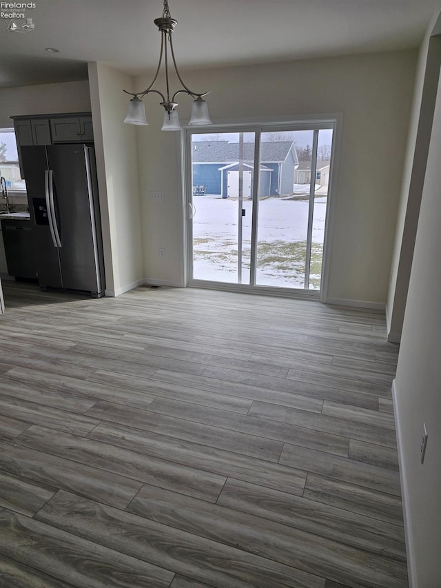 unfurnished dining area featuring a notable chandelier, a sink, wood finished floors, and baseboards