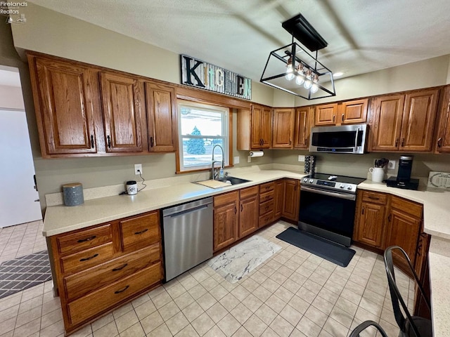 kitchen featuring brown cabinets, decorative light fixtures, stainless steel appliances, light countertops, and a sink