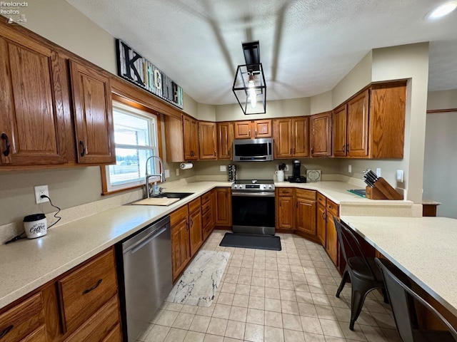 kitchen featuring light tile patterned floors, light countertops, appliances with stainless steel finishes, brown cabinetry, and a sink