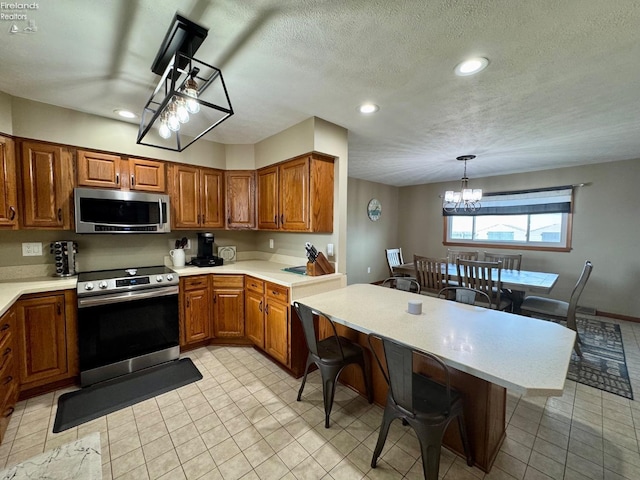 kitchen featuring stainless steel appliances, light countertops, brown cabinets, a kitchen bar, and pendant lighting