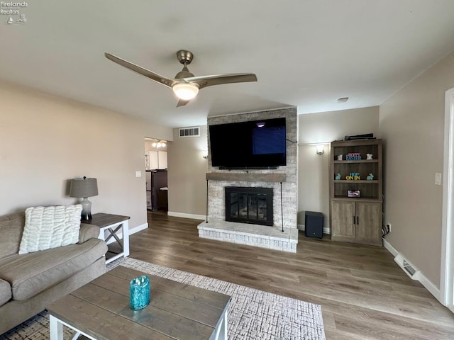 living area with a brick fireplace, wood finished floors, visible vents, and baseboards