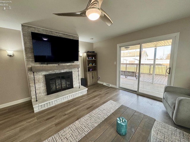 living room featuring baseboards, visible vents, a ceiling fan, wood finished floors, and a brick fireplace