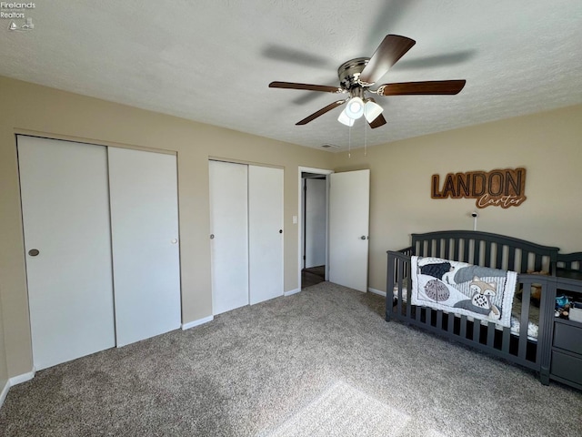 bedroom with a textured ceiling, carpet flooring, a ceiling fan, visible vents, and multiple closets