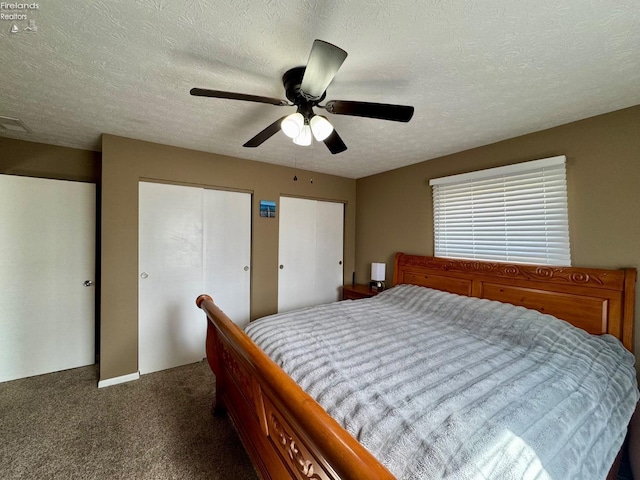 bedroom featuring two closets, visible vents, dark carpet, a ceiling fan, and a textured ceiling