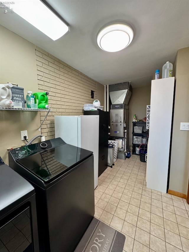 kitchen featuring refrigerator, light tile patterned floors, freestanding refrigerator, brick wall, and separate washer and dryer