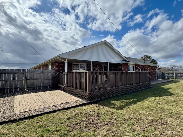 rear view of house with brick siding, a lawn, a patio, and fence