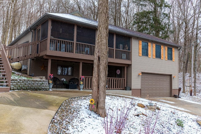 view of front of property with concrete driveway, a sunroom, a patio area, a garage, and stairs