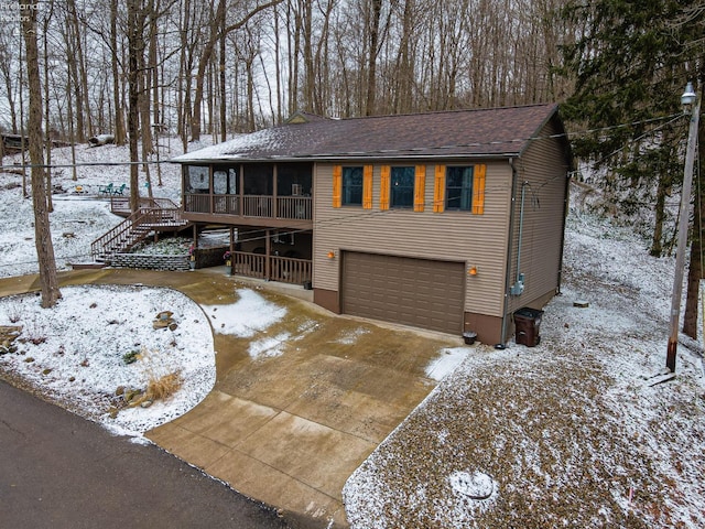 chalet / cabin with an attached garage, a sunroom, concrete driveway, roof with shingles, and stairway