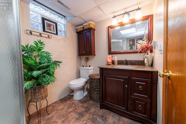 bathroom featuring toilet, visible vents, a drop ceiling, and vanity