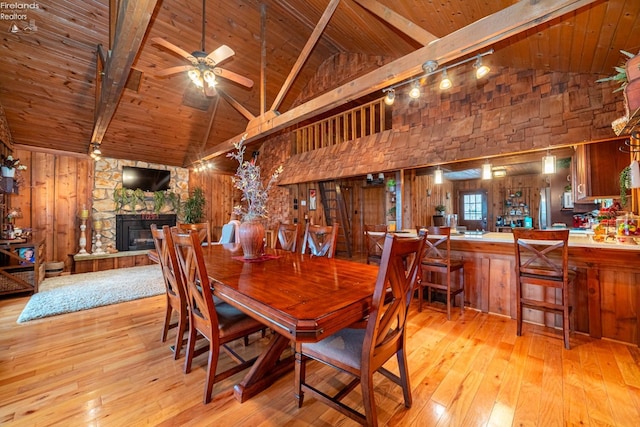 dining area with a stone fireplace, wood-type flooring, wooden ceiling, and a ceiling fan