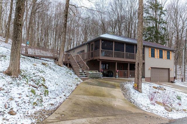 chalet / cabin with a garage, a sunroom, concrete driveway, stairway, and a wooden deck