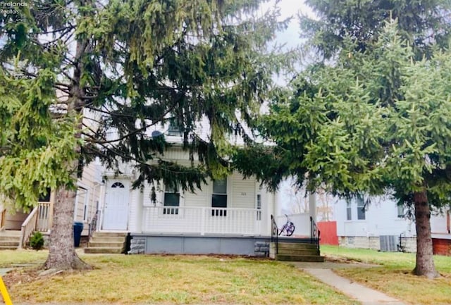 view of property hidden behind natural elements with a front yard, covered porch, and cooling unit