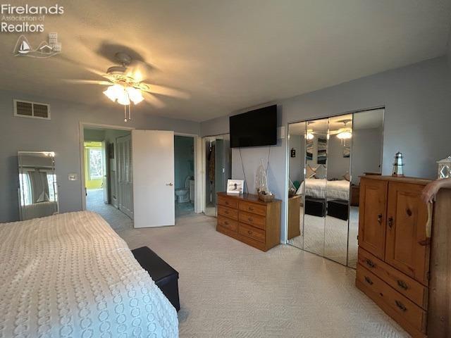 bedroom with light colored carpet, visible vents, ceiling fan, and two closets