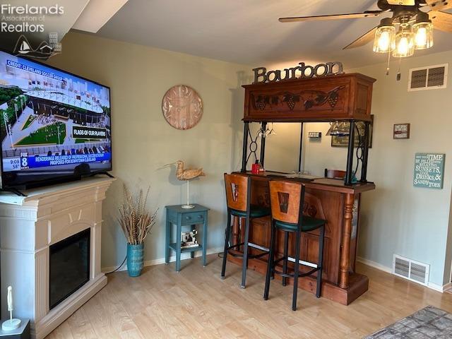 bar with a fireplace, wood finished floors, visible vents, and baseboards