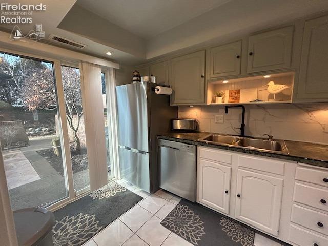 kitchen with stainless steel appliances, a tray ceiling, dark countertops, and a sink