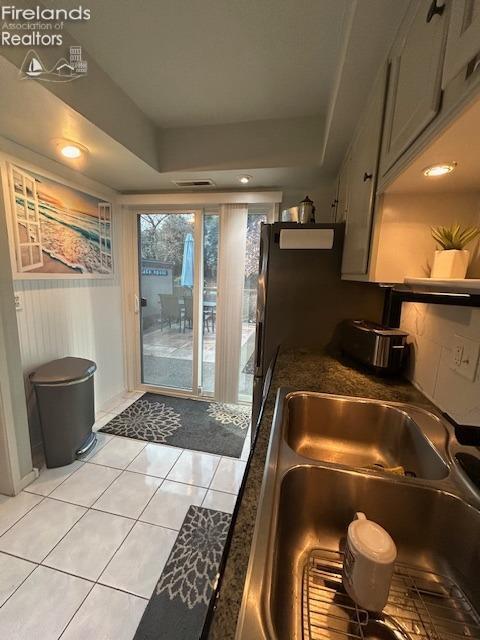 kitchen with light tile patterned floors, visible vents, dark countertops, a tray ceiling, and a sink