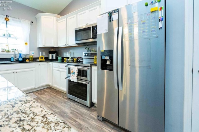 kitchen with light wood finished floors, dark countertops, appliances with stainless steel finishes, white cabinetry, and a sink