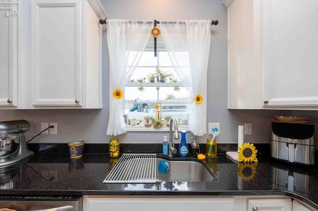 kitchen featuring dark stone countertops, white cabinets, and a sink