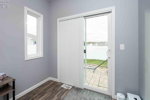 doorway with dark wood-style floors, visible vents, and baseboards