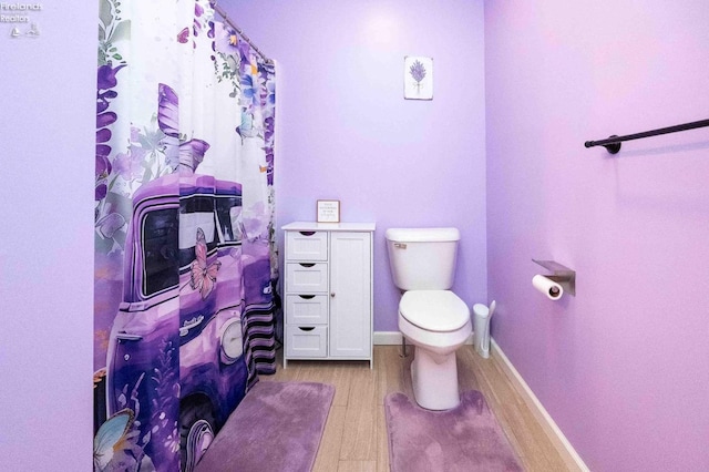 bathroom featuring toilet, baseboards, wood finished floors, and a shower with shower curtain