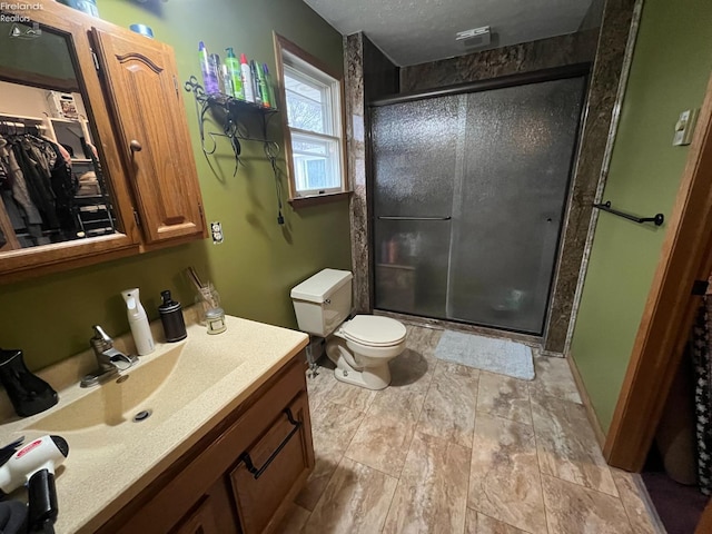 bathroom featuring a textured ceiling, toilet, vanity, a spacious closet, and a shower stall