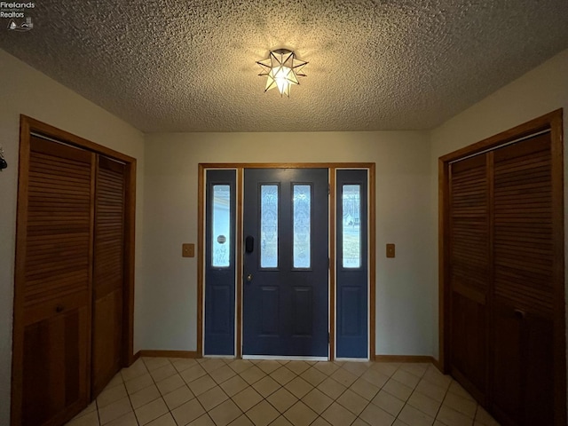 entryway with a textured ceiling, baseboards, and light tile patterned floors