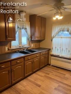 kitchen featuring radiator, light wood-style floors, dark countertops, and a ceiling fan