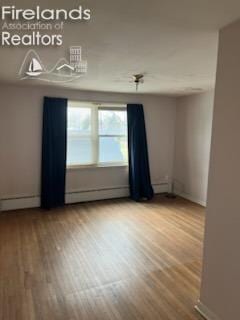 unfurnished room featuring baseboard heating and wood finished floors