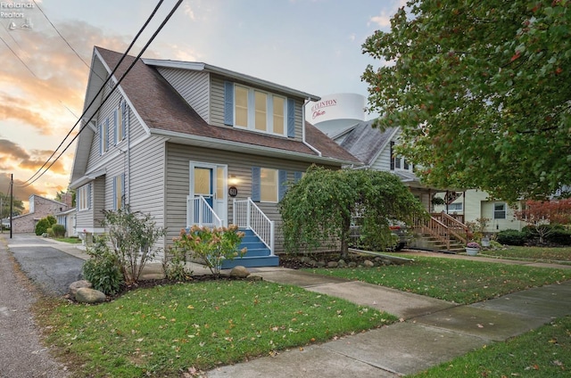 view of front of house with a shingled roof and a lawn