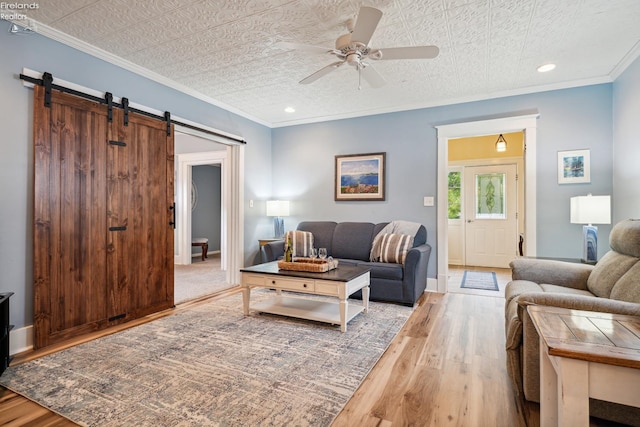 living area featuring a barn door, wood finished floors, a ceiling fan, and crown molding