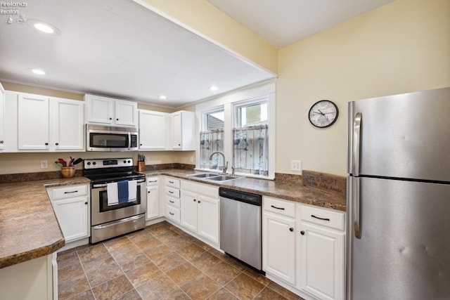 kitchen featuring stainless steel appliances, dark countertops, recessed lighting, white cabinetry, and a sink