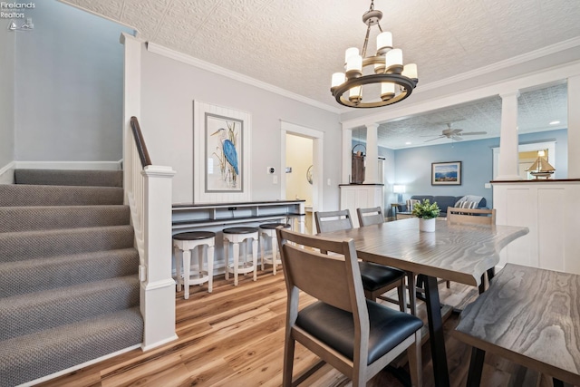 dining area featuring ornate columns, light wood-style flooring, stairway, and ceiling fan with notable chandelier