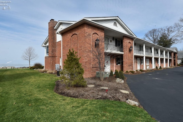 exterior space featuring driveway, a yard, a chimney, and brick siding